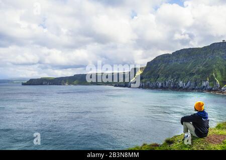 Ein junger Wanderer, der sich auf einem Wanderweg entlang der Küste von Antrim, Ulster, Nordirland, Großbritannien und Europa ausruhen kann Stockfoto