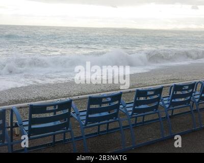 Eine Reihe leerer blauer Strandstühle mit Blick auf stürmische Meere an der Promenade des Anglais in Nizza, März 2020 Stockfoto