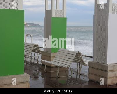 Grauer Himmel und stürmisches Meer Anfang März mit leeren Sitzplätzen an der Strandpromenade von Anglais in Nizza an der französischen Riviera. Stockfoto
