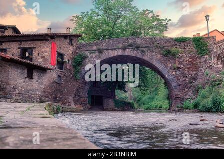 Die mittelalterliche Bogensteinbrücke von San Cayetano über den Fluss Quieviesa in Pobes, umgeben von mittelalterlichen Gebäuden, das Bild aus einem niedrigen Winkel Stockfoto