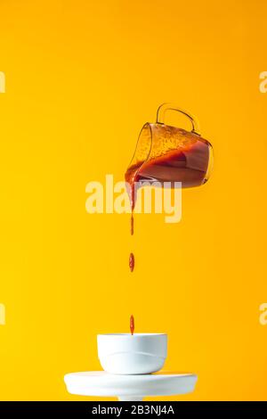 Sauce im Glasbecher, in der Luft gefroren. Gießen von hausgemachtem DIY Natural Konserven heiße Tomatensauce aus kleinem Glas in weißen Keramiktopf. Gelbes Essen Kunst Backgr Stockfoto