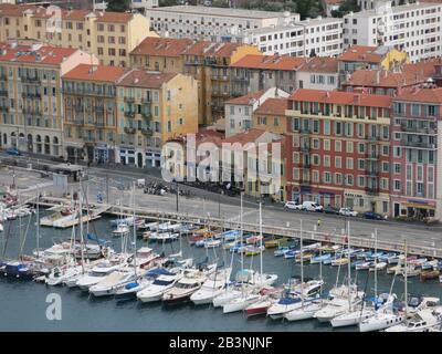 Blick auf den Hafen von Nizza an der französischen Riviera; Reihen von großen, teuren Yachten befinden sich in einem sicheren Hafen, der von hohen Stadthäusern übersehen wird. Stockfoto