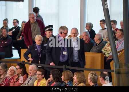 Edinburgh, Großbritannien. März 2020. Dargestellt: Ein Protestant wird am Ende der ersten Ministerfragen aus der Galerie in der Debattierkammer begleitet. Das Parlament wurde suspendiert, während das Protestor von der Polizei und der Sicherheit nach draußen begleitet wurde. Szenen aus ersten Ministerfragen im schottischen Parlament in Holyrood, Edinburgh. Kredit: Colin Fisher/Alamy Live News Stockfoto