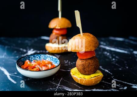 Hausgemachte mediterrane Mini Falafel Vegan Burger mit Tzatziki und Turmeric Sauce. Starteressen mit Holzstäbchen/Pico de Gallo Salat. Gesundes Organ Stockfoto