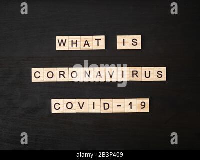 Was ist Coronavirus COVID-19 Wörter aus Holzblock. Was ist Coronavirus COVID-19 Text auf dramatischer Atmosphäre schwarzer Holztisch. Coronavirus Konzept Draufsicht. Stockfoto
