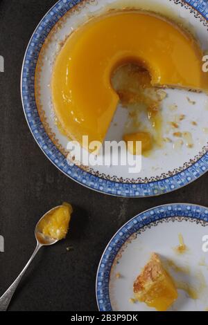 Große brasilianische Kokosnuss- und Eigelb-Pudding-Kuchen, genannt Quinim, auf einem weißen und blauen Teller mit einem Löffel Stockfoto