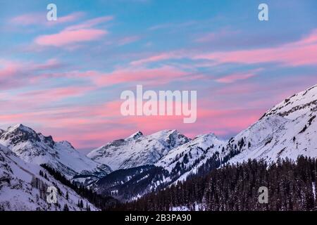 Rosafarbene Wolken liegen in einem blauen Himmel über einem schneebedeckten Alpenpanorama. Stockfoto