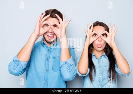 Fröhlicher glücklicher Mann und Frau, die mit den Fingern eine Brille machen und Zunge zeigen Stockfoto