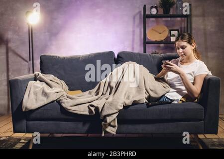 Ein junges Mädchen schreibt SMS am Telefon. Das Mädchen liegt auf der Couch. Gemütliches Zimmer. Stockfoto