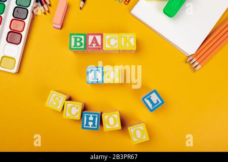 Zurück zum Schulkonzept. Farbige alphabetische Würfel aus Holz auf hellgelbem Hintergrund Stockfoto