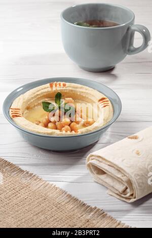 Arabisches Frühstück Hummusgericht mit Brot und einer Tasse heißen Minztee auf Holztisch Stockfoto