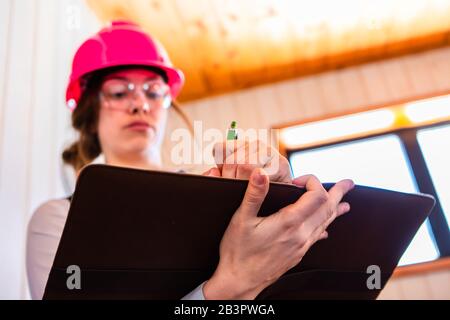 Selektiver Fokus, niedrige Winkelansicht des Hausinspektors mit Linkshänder, der Notizen, Rezensionen oder Berichte über den Hauszustand mit Hilfe einer Zwischenablage erstellt. Stockfoto