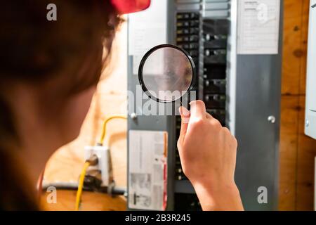 Selektive Fokussierung auf die Hand der Inspektorin, die eine Lupe an der Vorderseite der Hausverteilungsplatine hält. Überprüfung der Hauselektrik Stockfoto