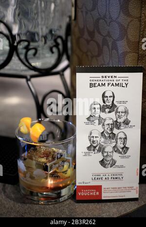 Ein Glas altmodischer Whiskey-Cocktail wird im serviert Bar in Jim Beam American Stillhouse neben einer Karte mit Porträts von 7 Generationen der Beam Familie beside.Clermont.Kentucky.USA Stockfoto