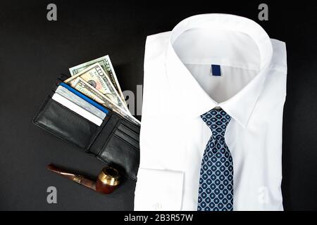 Hochwinkeliger Blick auf das gefaltete weiße Mannshirt mit Brieftasche und Rohr auf Schwarz Stockfoto