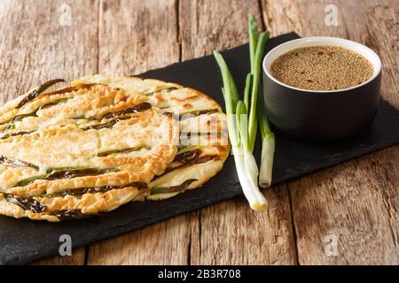 Traditionelle koreanische Pfannkuchen aus Pajeon mit grünen Zwiebeln auf einem Schieferbrett auf einem Tisch. Horizontal Stockfoto