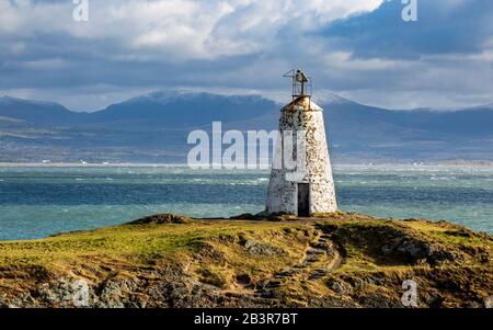 Der Leuchtturm Twr Bach auf der Insel Llanddwyn mit schneebedeckten Snowdonia Bergen im Hintergrund, Anglesey Stockfoto