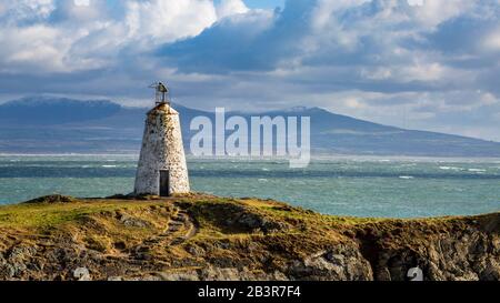 Der Leuchtturm Twr Bach auf der Insel Llanddwyn mit schneebedeckten Snowdonia Bergen im Hintergrund, Anglesey Stockfoto