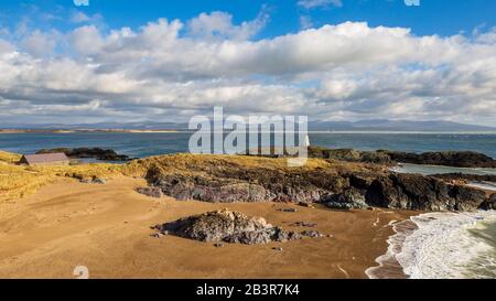 Ein Blick auf Twr Bach und die schneebedeckten Snowdonia Berge über Porth Twr Mawr auf Llanddwyn Island, Anglesey Stockfoto