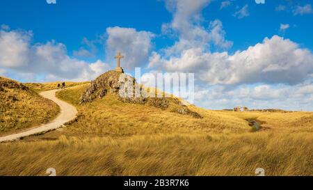 Ein Blick auf den Küstenweg und die Ruinen der St. Dwynwen Kirche und die modernen und keltischen Kreuze auf Llanddwyn Insel, Anglesey Stockfoto