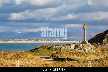 Das keltische Kreuz auf der Insel Llanddwyn mit den Sanddünen des Newborough Beach und den schneebedeckten Bergen von Snowdonia im Hintergrund, Anglesey Stockfoto