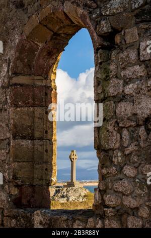 Das Keltenkreuz hat einen Blick durch die Ruinen von St Dwynwens Kirche auf der Insel Llanddwyn, Anglesey Stockfoto
