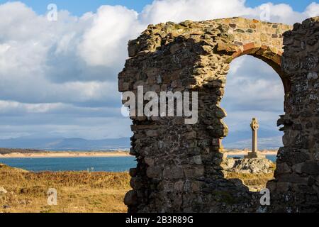 Das Keltenkreuz hat einen Blick durch die Ruinen von St Dwynwens Kirche auf der Insel Llanddwyn, Anglesey Stockfoto