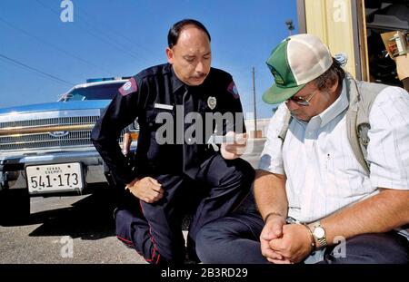 Austin, Texas, USA, 1996. Der hispanische Polizist liest Miranda Rights vor einem Verdächtigen in Handschellen vor. HERR ©Bob Daemmrich Stockfoto