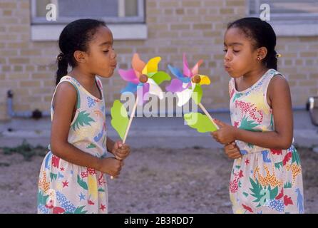 Austin Texas USA, um 1993: Acht Jahre alte schwarze Zwillingsschwestern blasen auf Nadelräder, um sie zum Drehen zu bringen.©Bob Daemmrich Stockfoto