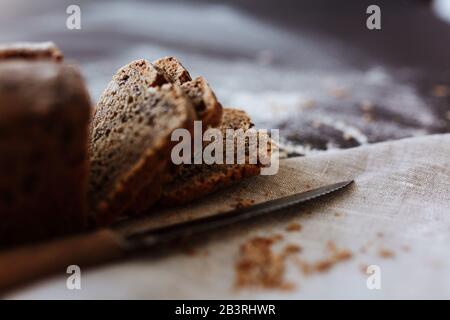 Laib des frisch gebackenen artisan Roggenbrot in Scheiben geschnitten auf Holz Schneidebrett mit Messer über Dunkelbraun Textur Hintergrund. Ansicht von oben, kopieren. Stockfoto