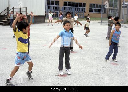 San Antonio, Texas USA, um 1992: Schulfinanzierungskrise in Texas -- Grundschüler springen während der Sportausbildung an der Frey School im chronisch unterfinanzierten Edgewood School District auf einer schlecht gewarteten Asphaltfläche Hampelmänner. ©Bob Daemmrich Stockfoto