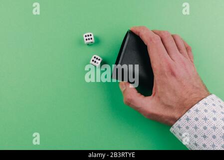 Hand eines Mannes, der mit dem Schüttler Würfel vor grünem Tischhintergrund rollt Stockfoto