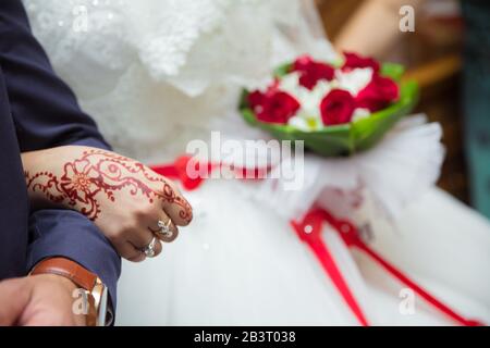 Kommen wir in die Arme des Bräutigam. Die Frau hält einen roten Blumenstrauß in der Hand. Hände und Finger werden auf Henna gezogen. Stockfoto
