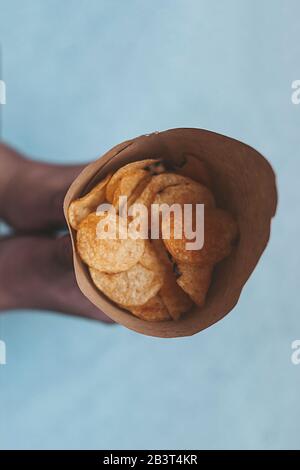 Frau, die einen Papierkegel voller Kartoffelchips hält. Draufsicht. Ansicht von oben Stockfoto