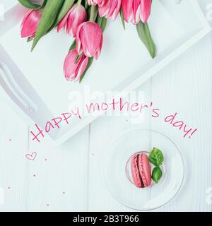 Glückwunschkarte für den Muttertag. Rosafarbene Federtulpen und Himbeer-Makaron auf weißem Hintergrund. Draufsicht Stockfoto