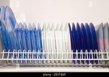 Teller in verschiedenen Farben im Tellertrockner im schrank auf weißem Hintergrund. Stockfoto