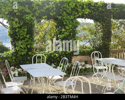 Tisch und Stühle auf einer schattigen Terrasse auf dem Gelände der Villa Ephrussi de Rothschild, einer der spektakulären Gärten der französischen Riviera. Stockfoto