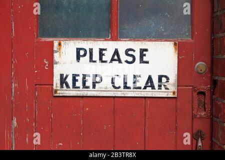 Altes und abgenutztes handgemaltes Schild "Bitte klar aufbewahren" an der alten abgenutzten roten Tür. Stockfoto