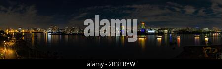 Ein Panoramabild der Bucht von Tokio mit der beleuchteten Regenbogenbrücke und den olympischen Ringen bei Nacht. Stockfoto