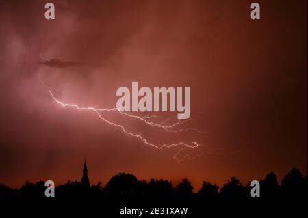 Regen fällt und Blitzschlag bei Gewitter nachts über Kirchturm und Bäume Stockfoto