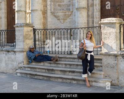 Frau, die vor einem mit einem Gatter versehenen Gebäude mit Bettler im Hintergrund steht, Havanna, Kuba Stockfoto