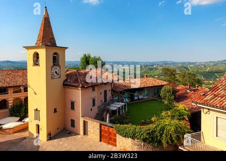 Blick auf die kleine Pfarrkirche, die Landhäuser und die grünen Weinberge auf den Hügeln vor dem blauen Himmel im Piemont, Norditalien. Stockfoto