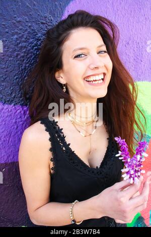 Junge Frau mit blauen Augen, die Blumen halten und vor der Kamera lachen. Stockfoto