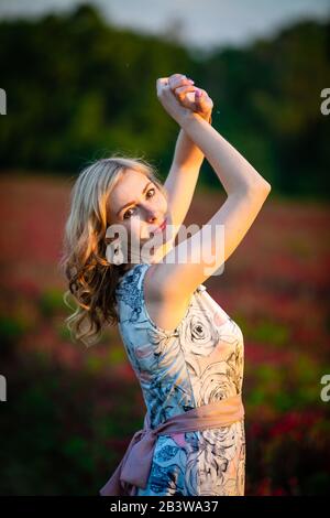 Junge Frau in rosafarbenem Kleid auf dem Feld des roten Kleeblatts in der Sonnenuntergangszeit Stockfoto