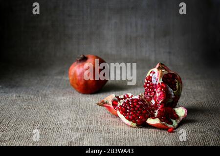 Rote Halbe Granatapfel und rohe Granatäpfel auf braunem Sacktuchhintergrund. Rustikaler Stil. Leckere Früchte, Vitaminkoktail Stockfoto