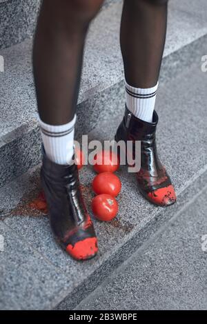 Urbaner Stil. Junge, stilvolle Frau in Hügeln und Socken, die die Treppe hinuntergehen und auf Tomaten treten, Füße nah oben Ansicht Stockfoto