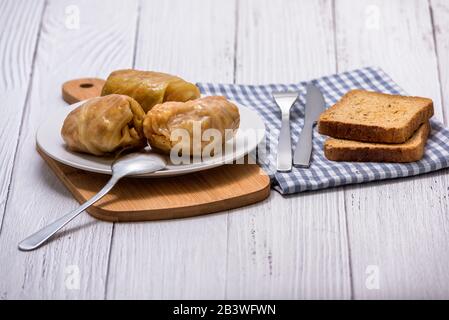 Kohlbrötchen mit Fleisch, Reis und Gemüse in einem weißen Teller auf einem Holztisch. Gefüllte Kohlblätter mit Fleisch. Sarma, Dolma, Chou farci, Golubtsy Stockfoto