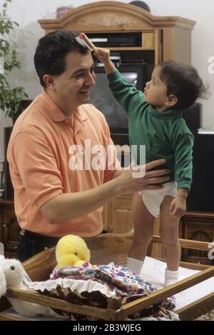 Austin Texas USA, 1995: Der hispanische Vater kleidet seine philippinisch-amerikanische Tochter, während ihre Mutter bei der Arbeit ist. ©Bob Daemmrich Stockfoto