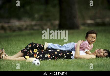 Austin, Texas, USA, 1995: Philippinisch-amerikanische Mutter und ihre 20 Monate alte Tochter spielen im Stadtpark im Gras. HERR ©Bob Daemmrich Stockfoto