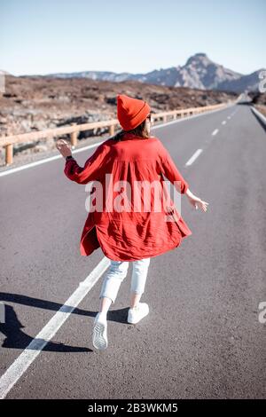 Frau stilvoll in Rot gekleidet auf der schönen Straße inmitten des vulkanischen Tals, Blick von der Rückseite. Sorgloses Lifestyle- und Reisekonzept Stockfoto